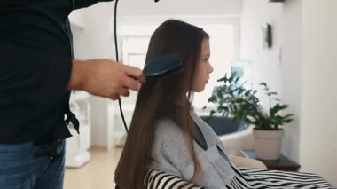 Profesyonel kuaför güzel bir kızın uzun kahverengi saçlarını ustalıkla kuruturken aynı zamanda canlı bir güzellik salonunda uzman saç bakım hizmeti veriyor.