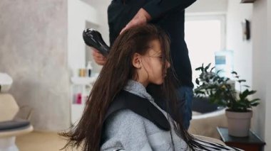 Profesyonel kuaför güzel bir kızın uzun kahverengi saçlarını ustalıkla kuruturken aynı zamanda canlı bir güzellik salonunda uzman saç bakım hizmeti veriyor.