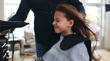 Profesyonel kuaför güzel bir kızın uzun kahverengi saçlarını ustalıkla kuruturken aynı zamanda canlı bir güzellik salonunda uzman saç bakım hizmeti veriyor.