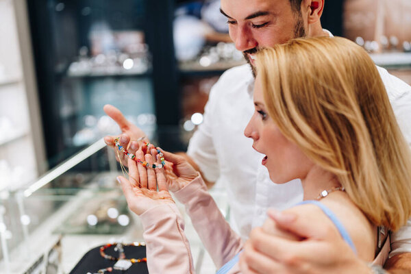 Happy couple enjoying a moment in a jewelry store, selecting a beautiful jewelry pieces together. Both are happy and smiling with love and excitement.