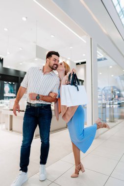 Mutlu genç çift, bir alışveriş merkezinden lüks bir mağazadan zarif mücevherler aldıktan sonra alışveriş merkezlerinde gezinirken bir öpücüğü paylaşıyor.