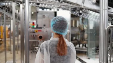 Koruyucu giysiler ve maske takan kadın kalite kontrol müfettişi su şişeleme fabrikasındaki üretim hattını incelerken panoya notlar yazıyor.