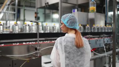 Koruyucu giysiler ve maske takan kadın kalite kontrol müfettişi su şişeleme fabrikasındaki üretim hattını incelerken panoya notlar yazıyor.