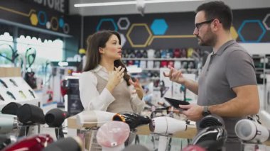 Neşeli bir elektronik mağazasında çeşitli ürünler sergilerken hamile bir müşteriye ev aletleri seçmesinde yardımcı olan gülümseyen mağaza asistanı