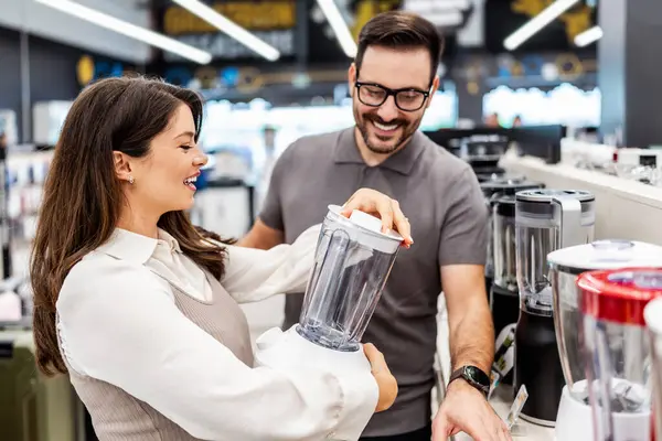 Neşeli bir elektronik mağazasında çeşitli ürünler sergilerken hamile bir müşteriye ev aletleri seçmesinde yardımcı olan gülümseyen mağaza asistanı