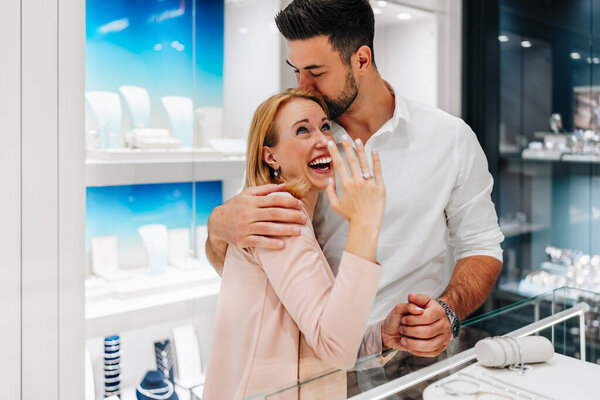 Happy couple enjoying a moment in a jewelry store, selecting a beautiful jewelry pieces together. Both are happy and smiling with love and excitement.