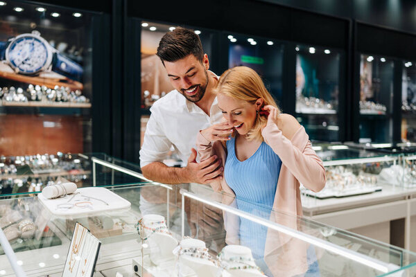 Happy couple enjoying a moment in a jewelry store, selecting a beautiful jewelry pieces together. Both are happy and smiling with love and excitement.