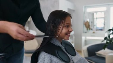 Profesyonel kuaför güzel bir kızın uzun kahverengi saçlarını makas ve tarak kullanarak ustaca keserken aynı zamanda canlı bir güzellik salonunda uzman saç bakım hizmeti veriyor.