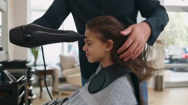 Profesyonel kuaför güzel bir kızın uzun kahverengi saçlarını ustalıkla kuruturken aynı zamanda canlı bir güzellik salonunda uzman saç bakım hizmeti veriyor.