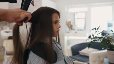 Profesyonel kuaför güzel bir kızın uzun kahverengi saçlarını ustalıkla kuruturken aynı zamanda canlı bir güzellik salonunda uzman saç bakım hizmeti veriyor.