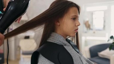 Profesyonel kuaför güzel bir kızın uzun kahverengi saçlarını ustalıkla kuruturken aynı zamanda canlı bir güzellik salonunda uzman saç bakım hizmeti veriyor.