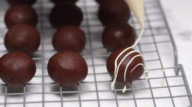 Pasta şefi lezzetli siyah çikolata toplarını serinletici rafta beyaz çikolata parçacıklarıyla süslemek için boru torbası kullanıyor.