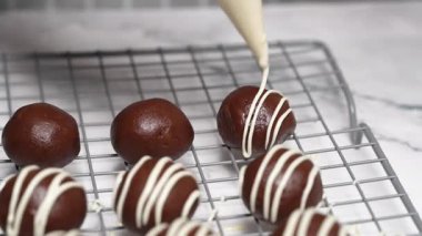 Pasta şefi lezzetli siyah çikolata toplarını serinletici rafta beyaz çikolata parçacıklarıyla süslemek için boru torbası kullanıyor.