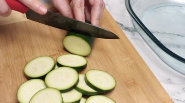 Şef bambu kesme tahtasının üzerinde taze kabak dilimliyor, profesyonel mutfak ortamında besleyici bir yemek için ustalıkla malzemeler hazırlıyor.