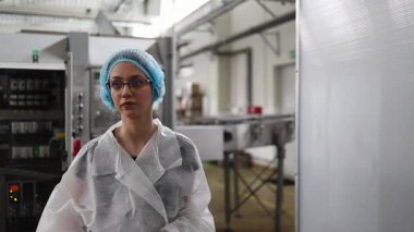 Koruyucu giysiler ve maske takan kadın kalite kontrol müfettişi su şişeleme fabrikasındaki üretim hattını incelerken panoya notlar yazıyor.