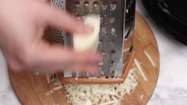 Ahşap kesim tahtasında peynir rendelemek, modern bir mutfakta leziz çelik aletler ve mermer aksanlarla dolu bir gurme yemeği için ustalıkla hazırlamak.