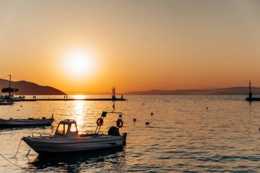 Küçük motorlu tekneler, sakin ve huzurlu bir atmosfer yaratarak, güzel bir altın gün batımı sırasında, rıhtımın yakınındaki sakin deniz suyunda yavaşça sallanıyorlar.