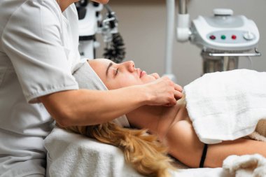 Profesyonel güzellik uzmanı masaj masasında uzanan kadın müşteriye nazikçe masaj yapıyor. Rahatlatıcı ve gençleştirici cilt bakımı sağlıyor.