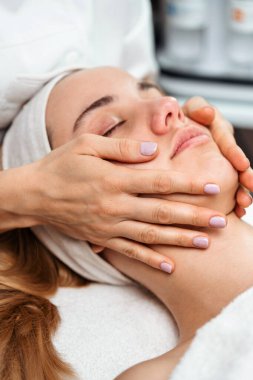 Profesyonel güzellik uzmanı masaj masasında uzanan kadın müşteriye nazikçe masaj yapıyor. Rahatlatıcı ve gençleştirici cilt bakımı sağlıyor.