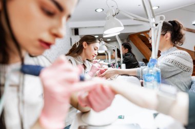 Modern bir güzellik salonunda çalışan profesyonel manikürcüler. Tatmin olmuş kadın müşteriler kaplıca merkezinde manikür tedavisi görüyor..