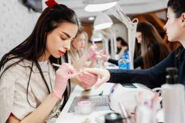 Modern bir güzellik salonunda çalışan profesyonel manikürcüler. Tatmin olmuş kadın müşteriler kaplıca merkezinde manikür tedavisi görüyor..