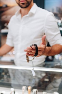 Beyaz gömlekli zarif iş adamı, vitrinin parlak ışıkları altında sergilenen saatleri dikkatle inceleyerek kuyumcudan yeni bir lüks saat seçiyor.