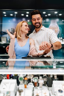 Zarif bir çift kuyumcuda eğleniyor, gülümseyip kucaklaşırken lüks saatler deniyorlar, özel bir durum için düşünceli bir satın alma kararı veriyorlar.