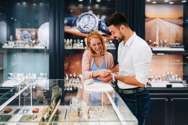 Elegant couple enjoying a moment in a jewelry store, trying on luxury watches while smiling and embracing, making a thoughtful purchase decision for a special occasion