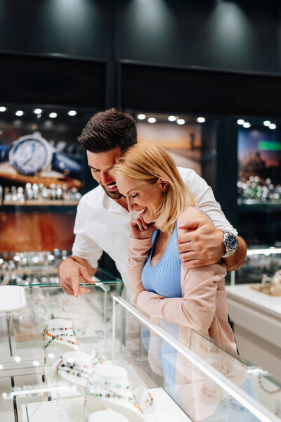 Elegant couple enjoying a moment in a jewelry store, trying on luxury watches while smiling and embracing, making a thoughtful purchase decision for a special occasion