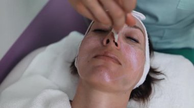 Profesyonel güzellik uzmanı gevşemiş bir müşterinin yüzüne nazikçe kremsi bir maske takarak sağlıklı cilt için rahatlatıcı ve canlandırıcı bir spa tedavisi uyguluyor.