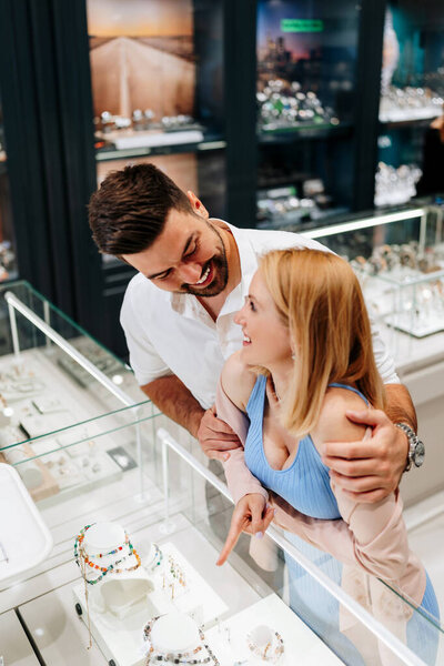 Happy young couple enjoying choosing and buying luxurious jewelry in jewelry store. Woman is happy and excited