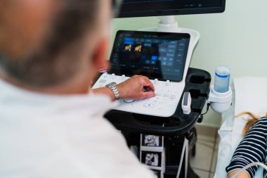 Jinekolog, hamile kadını muayene etmek için modern ultrason tarayıcısı kullanıyor. Klinikteki 4D fetüs görüntülerini gözlemliyor. Doğum öncesi teşhisi koyuyor.