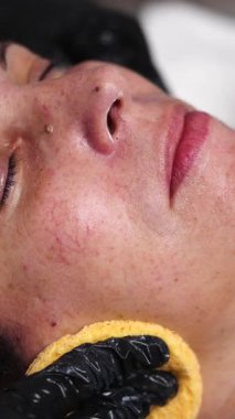 Cosmetologist using cotton pads for cleansing skin of beautiful mature woman during beauty treatments in salon. Wellness and facial care concept.