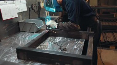 Koruyucu maske ve eldiven takan endüstriyel işçiler bir atölyede metal bir yapıyı kaynak yaparak yüksek sıcaklıktaki yay sürecinden parlak ışıklar ve kıvılcımlar yaratıyor.