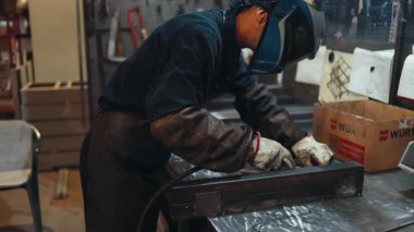 Koruyucu maske ve eldiven takan endüstriyel işçiler bir atölyede metal bir yapıyı kaynak yaparak yüksek sıcaklıktaki yay sürecinden parlak ışıklar ve kıvılcımlar yaratıyor.