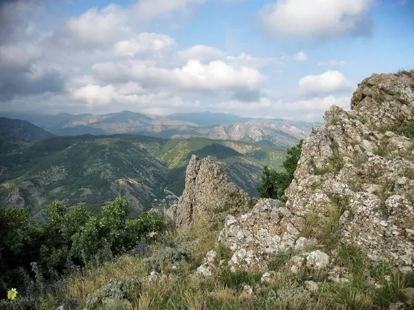    Dağlarla ve kayalarla kaplı bir manzara Mavi gökyüzünün altında bulutlarla.                         