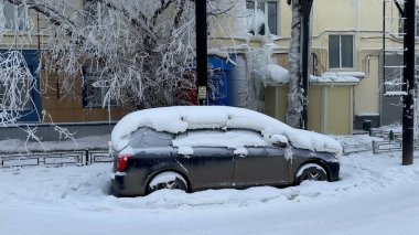 Sert bir kış boyunca bir araba tamamen donmuş bir caddede kar ve buzla kaplıdır. Ağaçlar, binalar ve çevresi dondurucu soğukla kaplanmış, yoğun bir soğuk hava manzarası sergiliyor.