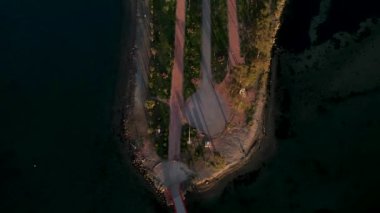 Gün batımında deniz ve lagün ile çevrili yürüme ve sürüş yolları olan kırmızı yaya köprüsü ve İnciralti şehir ormanının hava yatay görüntüsü.