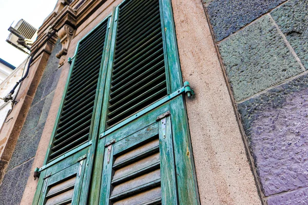 Yakından bakınca, taştan bir evin turkuaz ahşap panjuru görünüyor.