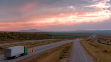Sunset Drive: Desert Steppe 'de yarı kamyonlar. Yüksek kalite 4K görüntü. Gün batımında uçsuz bucaksız çöl bozkırlarında yol boyunca ilerleyen bir tırın görüntüsü. Ulaşım. Taşımacılık Şirketi.