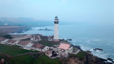 Yağmurlu kıyı havasında okyanus kıyısındaki deniz feneri. Yüksek kalite 4K görüntü. Yağmurlu, bulutlu kıyı havasının ortasında sabit bir deniz feneri kıyıda dimdik durur.. 