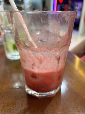 Kısmen tüketilmiş bir çilek suyu yüzeyinde yoğunlaşma olan bir bardakta oturur ve içeceklerin canlı pembe rengini gösterir.. 