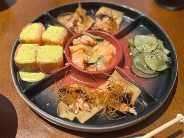 İçinde çeşitli dürüm, sashimi ve süslemeler bulunan lezzetli bir suşi tabağı. İçinde krem soslu taze somon, taze sebzeler ve çıtır çıtır kızarmış bir son var. Hepsi zarif, siyah bir tepside dizilmiş..