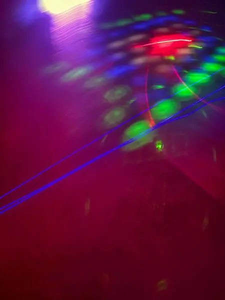 Bir gece partisinde renkli ışıkların hareketini gösteren soyut bir görüntü. Yeşil, mavi ve kırmızı ışıklar canlı bir ortamı aydınlatarak, karanlık bir arkaplana karşı lazer efektleriyle bir eğlence ve kutlama atmosferi yaratırlar..