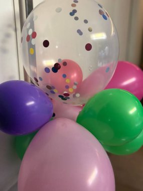 Değişik renklerde konfeti dolu şeffaf bir balon da dahil olmak üzere renkli balonların canlı bir bileşimi. Pembe, mor, yeşil ve eğlencenin neşeli paleti kutlamaları ve eğlenceyi çağrıştırıyor. Doğum günleri ve özel etkinlikler için mükemmel..