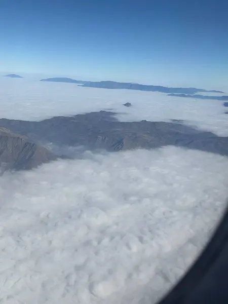 Dağları ve vadileri kaplayan yoğun bulutların nefes kesici hava manzarası. Uzaktan görünen zirveleri var. Açık mavi gökyüzü bu sakin sahneyi tamamlıyor, açık bir günde doğanın güzelliğini yakalıyor..
