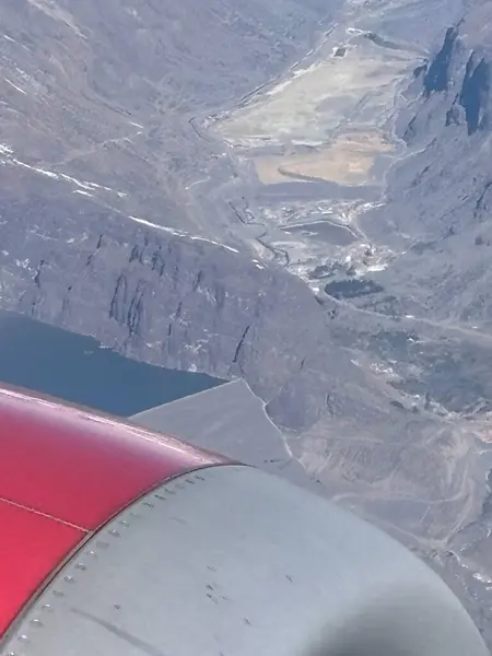 Etkileyici bir hava manzarası engebeli dağların ve derin bir gölün güzelliğini ön planda kırmızı bir uçak kanadı ile yansıtıyor, doğanın ve insan yaratıcılığının enginliğini gösteriyor..