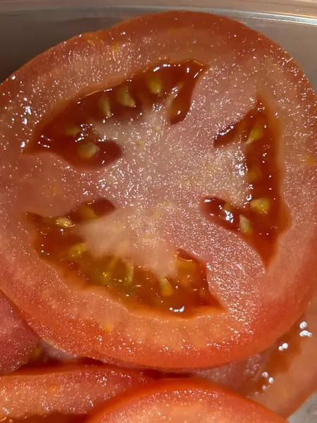 Taze domates dilimleri, sulu posasını ve görünür tohumlarını sergiliyor, salatalar, sandviçler ve sağlıklı yemekler için mükemmel. Resim dokuyu ve canlı kırmızı rengi vurgular.