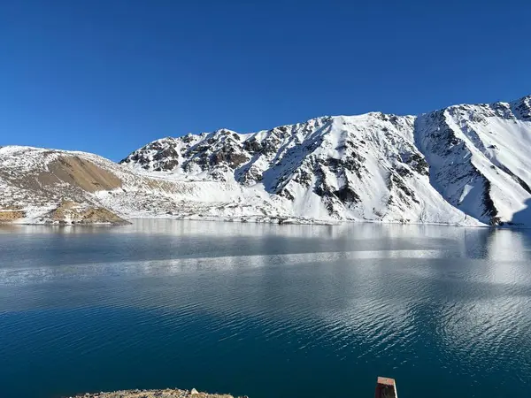 Karla kaplı güzel bir dağda donmuş bir gölün çarpıcı manzarası. Açık mavi gökyüzü sakin sulara yansıyarak sakin ve sakin bir atmosfer yaratır. Yükselen dağlar ihtişam ve doğal güzellik ekler..