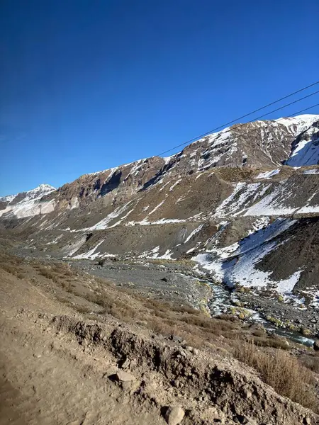 Etkileyici bir dağ manzarası derin vadiler ve açık mavi gökyüzünün altında karla kaplı tepeler. Sarmal nehir, güneş ışığını kayaların ve seyrek bitki örtüsünün arasında yansıtır. Huzuru ve doğal güzelliği çağrıştırır..